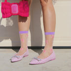 [lf] Model stands wearing sheer white socks with pink bows and purple cuffs.