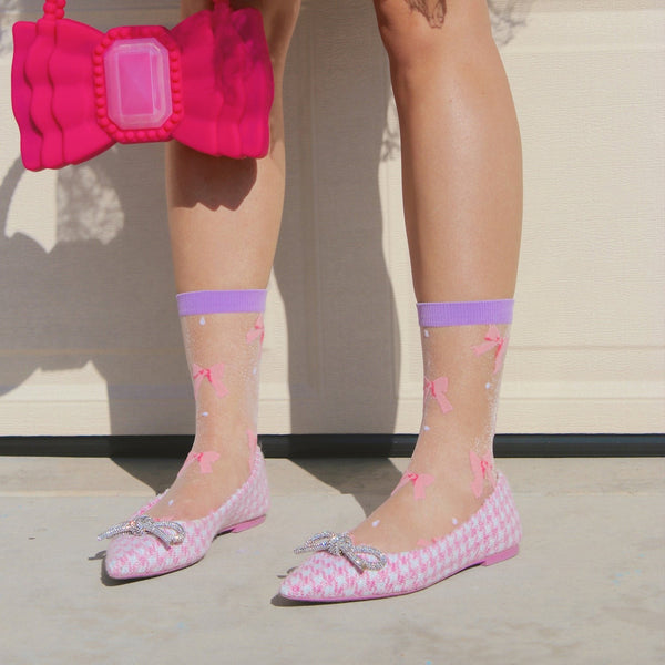 [lf] Model stands wearing sheer white socks with pink bows and purple cuffs.