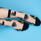 [lf] Legs crossed, wearing sheer socks with black cats in green plants and purple pots.
