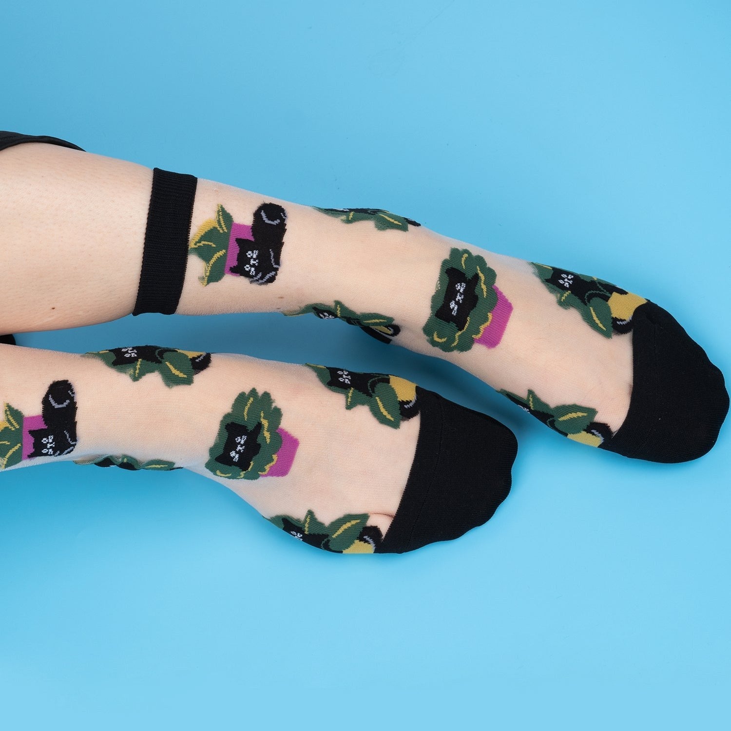 [lf] Legs crossed, wearing sheer socks with black cats in green plants and purple pots.