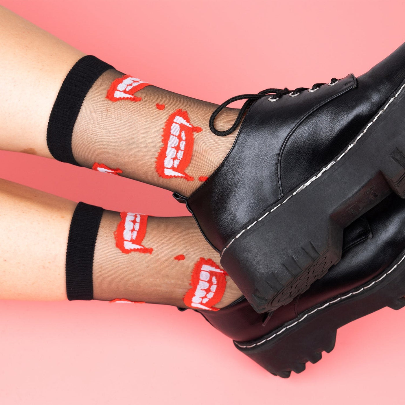 [lf] Legs crossed, model wears sheer black socks with red vampire teeth, paired with black platform shoes.
