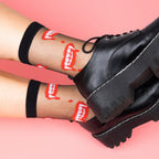 [lf] Legs crossed, model wears sheer black socks with red vampire teeth, paired with black platform shoes.