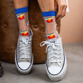 [lf] Model seated, wearing sheer socks with colorful abstract patterns and blue cuffs.