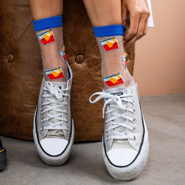 [lf] Model seated, wearing sheer socks with colorful abstract patterns and blue cuffs.