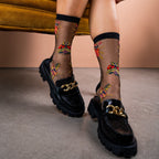 [lf] Legs in black sheer bug-patterned socks and chunky loafers on a concrete floor.
