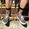 [lf] Legs dangle, showcasing tan socks with dark Bigfoot patterns and gray sneakers.