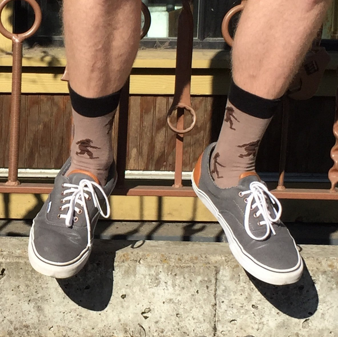 [lf] Legs dangle, showcasing tan socks with dark Bigfoot patterns and gray sneakers.