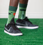 [lf] Person standing on green turf wearing green alien abduction socks and black sneakers.