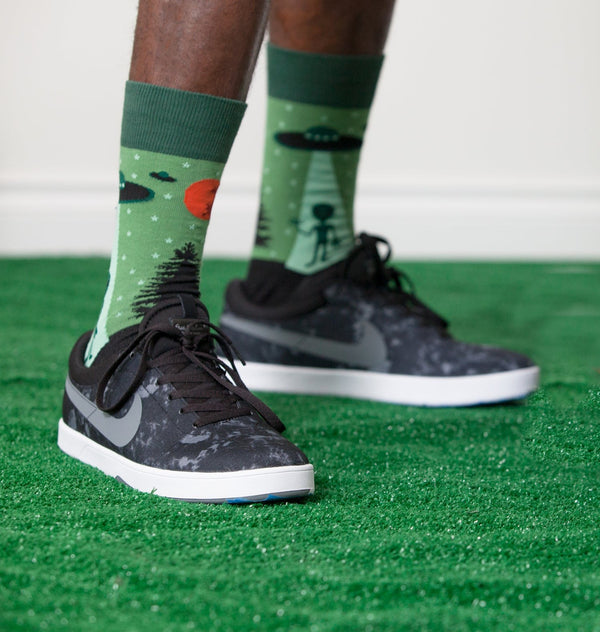 [lf] Person standing on green turf wearing green alien abduction socks and black sneakers.
