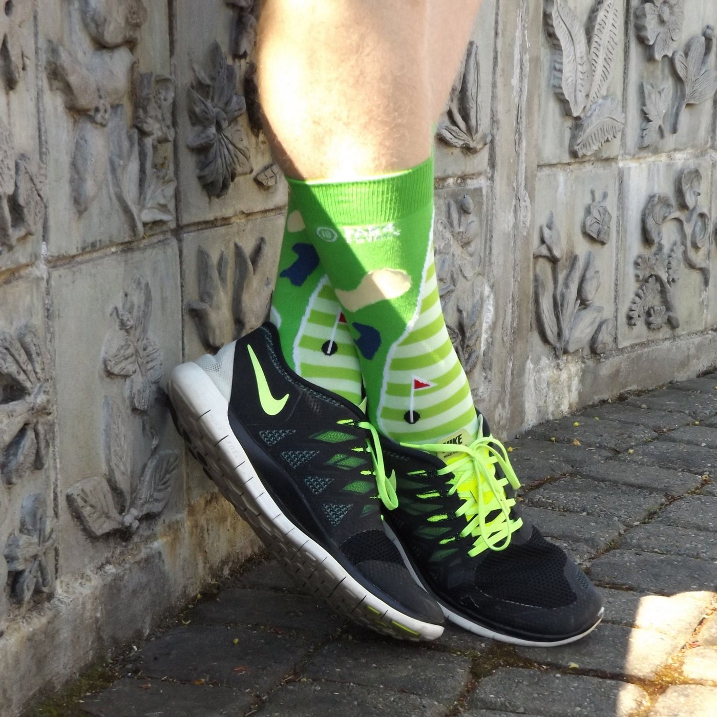 [lf] Person leaning against a carved wall, wearing green golf-themed socks and black sneakers.