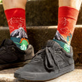 [lf] Person wearing red dinosaur and volcano socks with black sneakers on concrete steps.