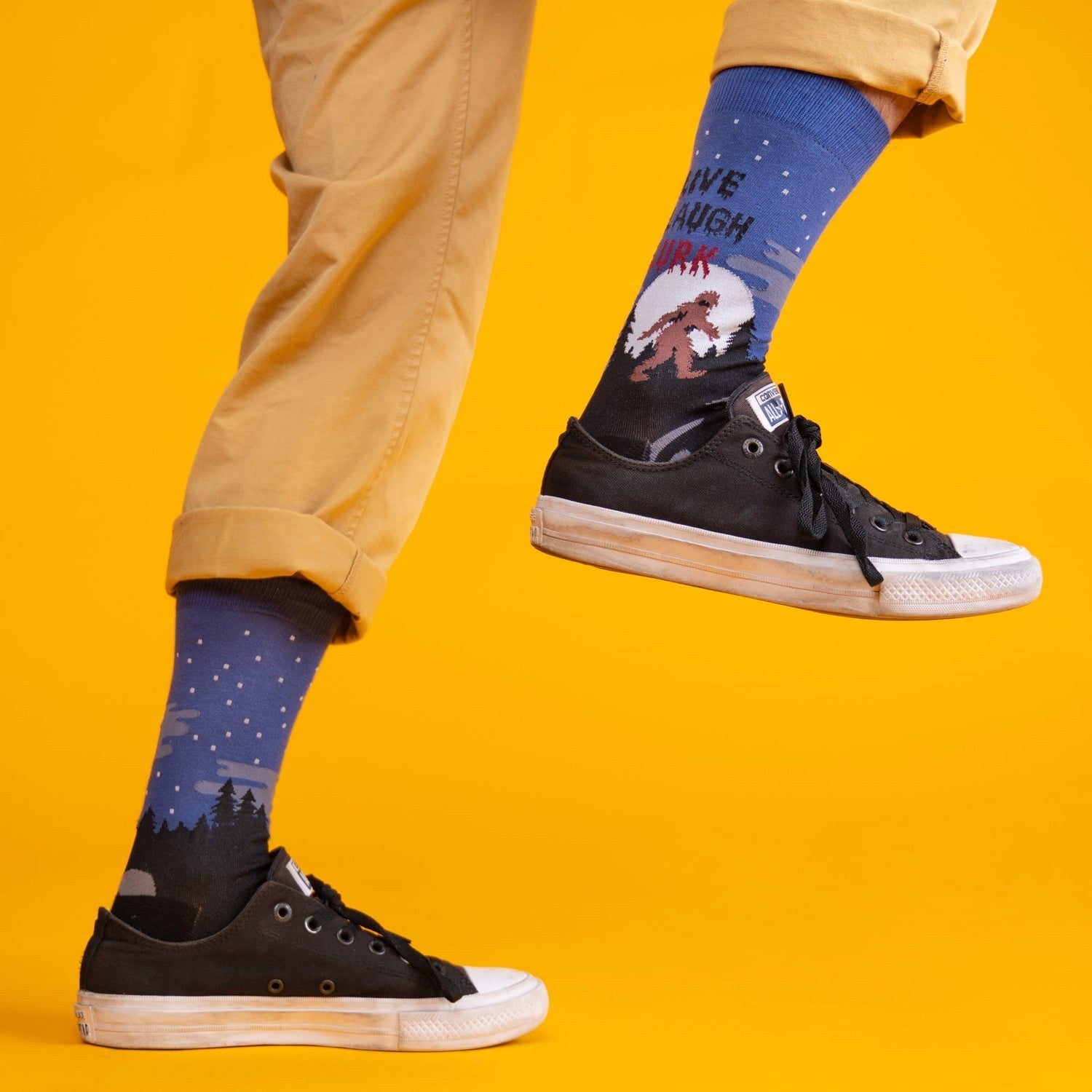 [lf] Person in tan pants and black sneakers, wearing blue Bigfoot socks with a starry night scene.