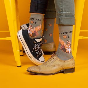 [lf] Two people wearing olive green squirrel and acorn socks with different shoes on a yellow floor.