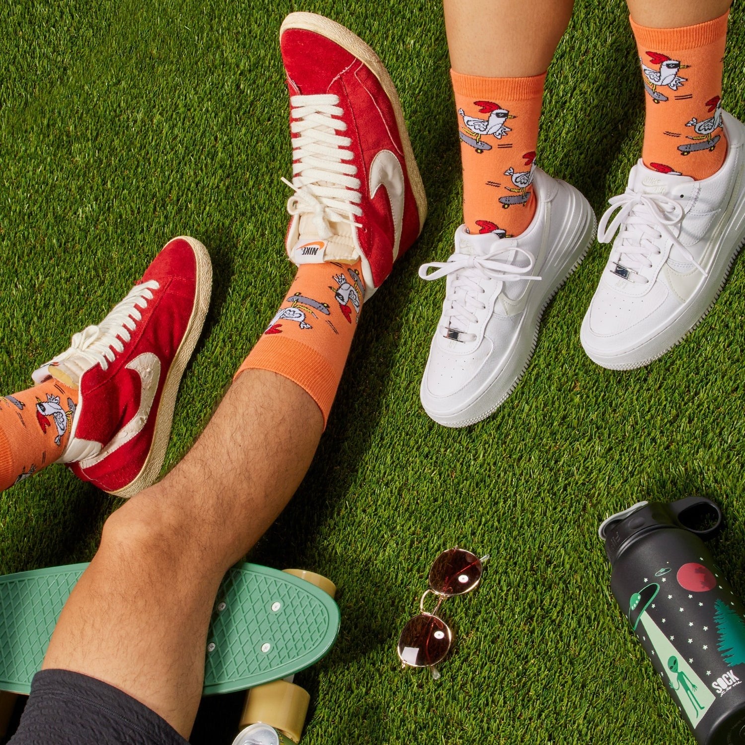 [lf] Legs on artificial grass, wearing orange socks with skateboarding chickens and red and white sneakers.