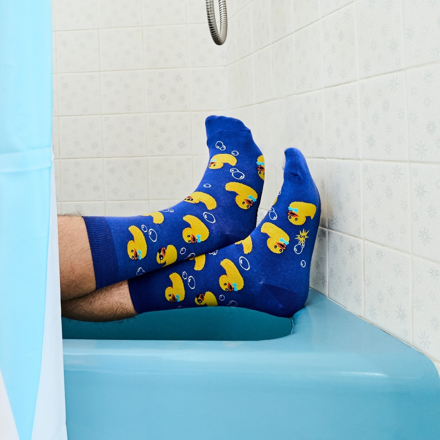 [lf] Feet in blue rubber duck socks relax on a tub edge, shower curtain visible.