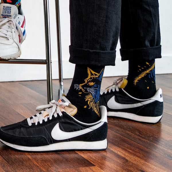 [lf] Person wearing black cat socks with yellow and blue accents, black pants, and sneakers.