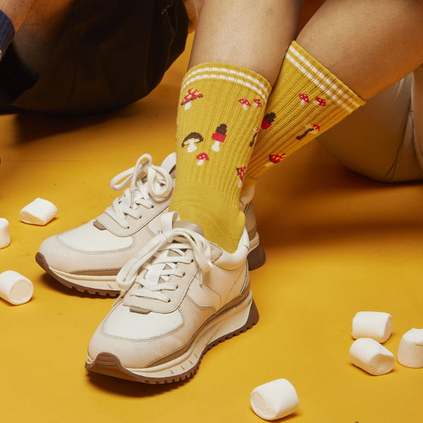 [lf] Yellow mushroom-patterned socks with white stripes worn by a seated model on a yellow floor.