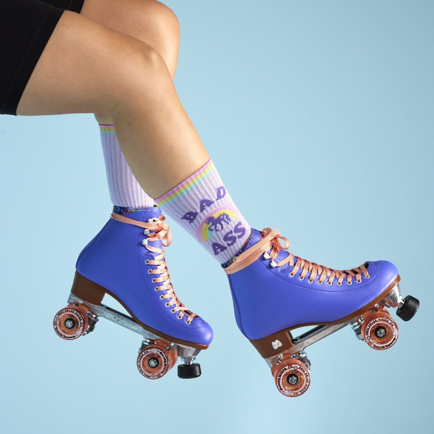 [lf] Legs in purple roller skates and rainbow "BAD ASS" socks against a blue background.