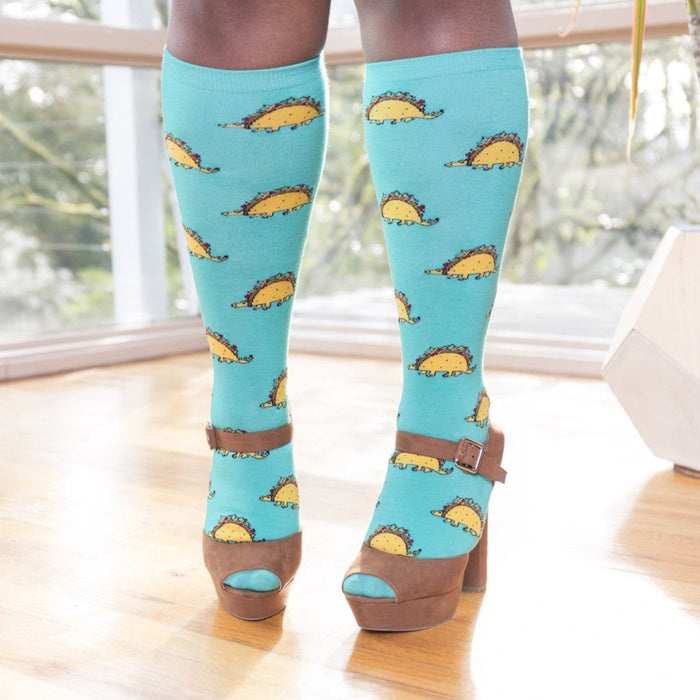 [lf] Model stands wearing blue knee-high socks with taco dinosaur pattern and brown platform heels.