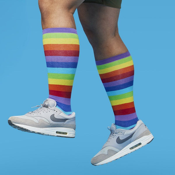 [lf] Person in grey sneakers and rainbow striped socks mid-stride against a blue background.