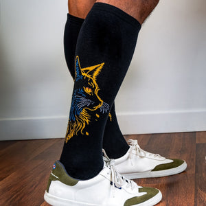 [lf] Person standing, wearing black socks with a yellow and blue cat design, and white sneakers.