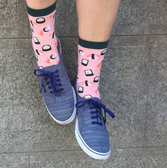 [lf] Legs in blue sneakers and pink sushi-patterned socks stand on a concrete surface.