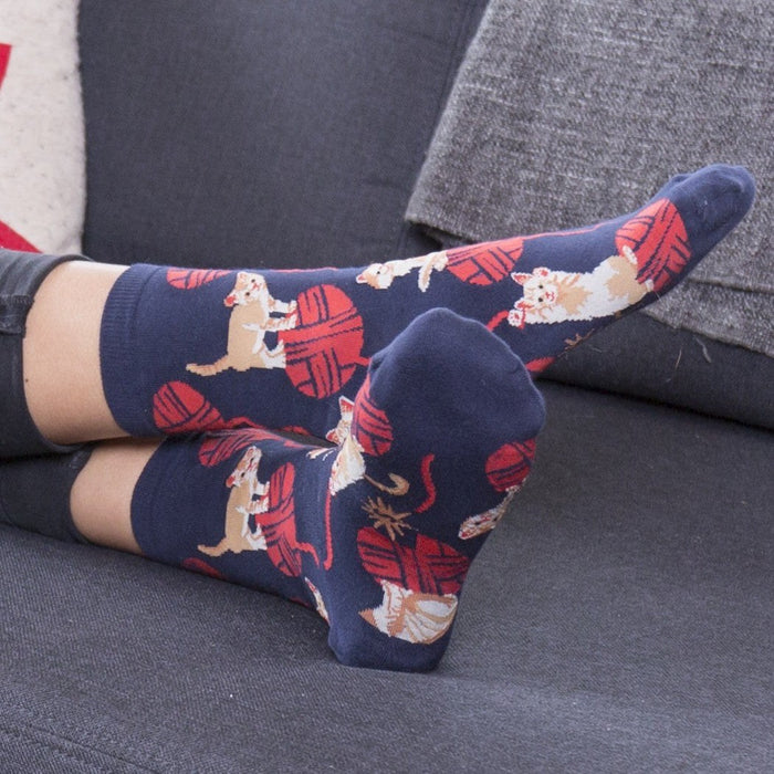 [lf] Feet in navy socks with playful cats and red yarn balls, relaxing on a gray couch.