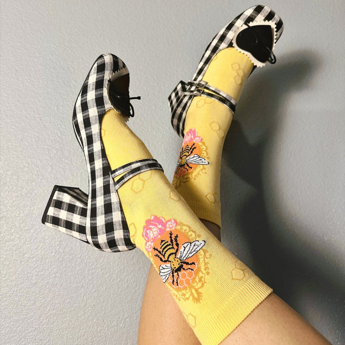 [lf] Legs crossed, yellow bee socks with black and white gingham Mary Jane heels.