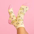 [lf] Feet in yellow and pink butter-patterned socks crossed against a pink background.
