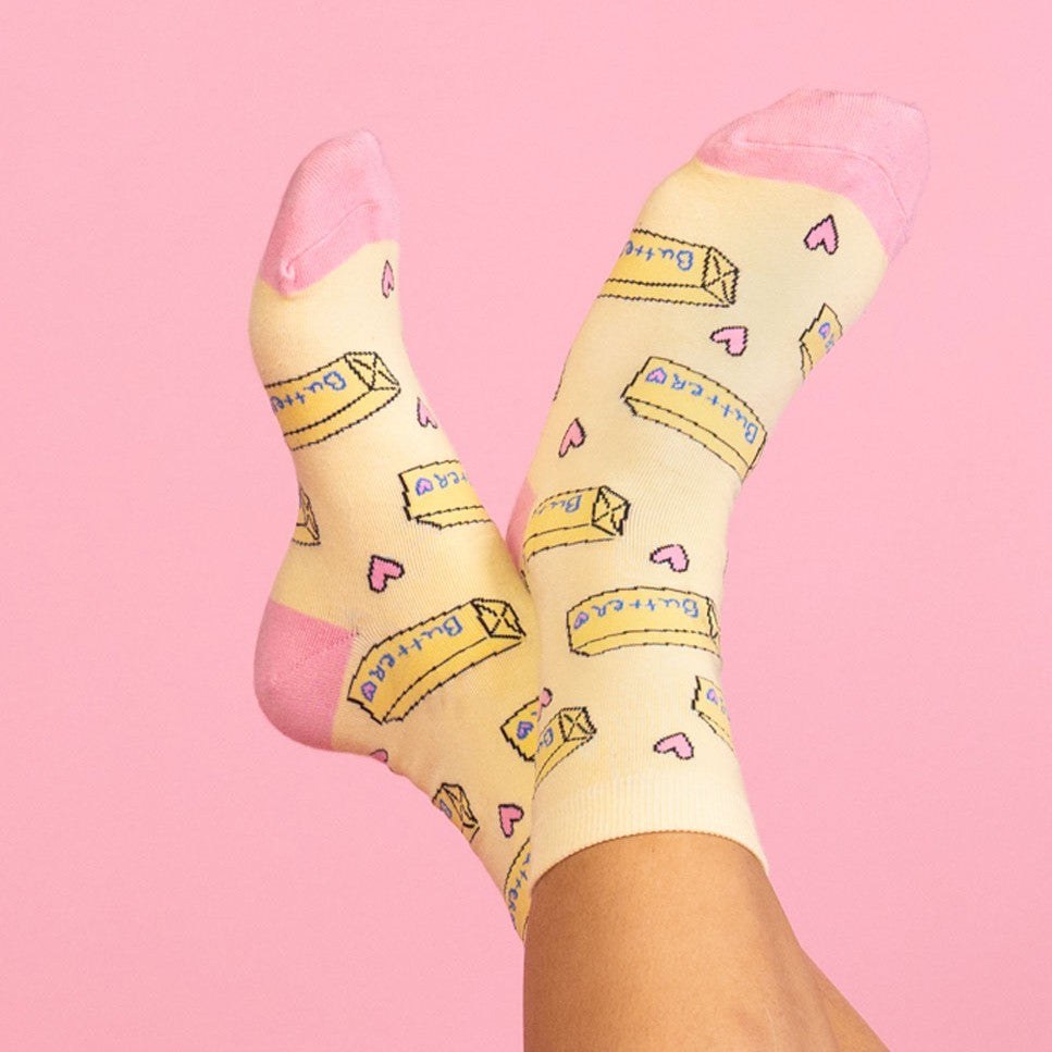 [lf] Feet in yellow and pink butter-patterned socks crossed against a pink background.