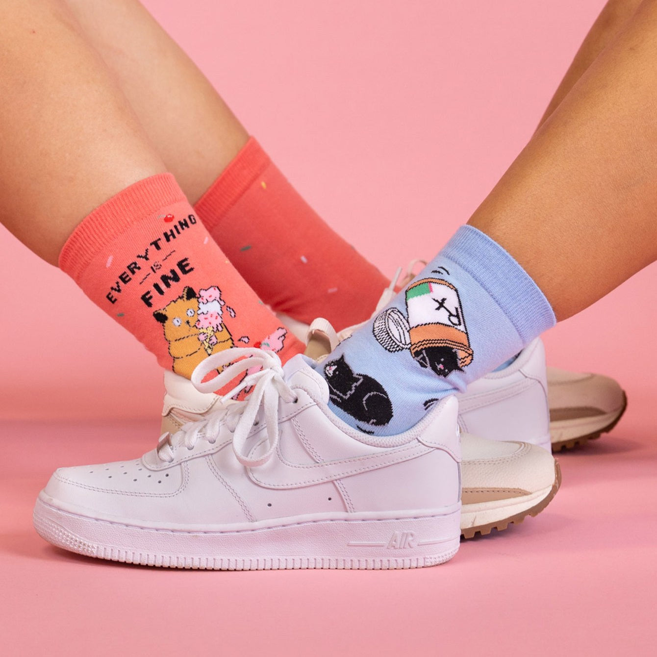 [lf] Two pairs of legs in colorful, patterned socks and sneakers on a pink background.