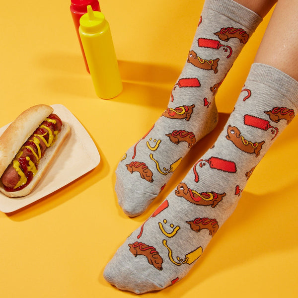 [lf] Feet in gray hot dog pattern socks next to a hot dog and condiment bottles.
