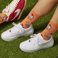 [lf] Legs in orange chicken-on-skateboard socks and white sneakers on green turf.