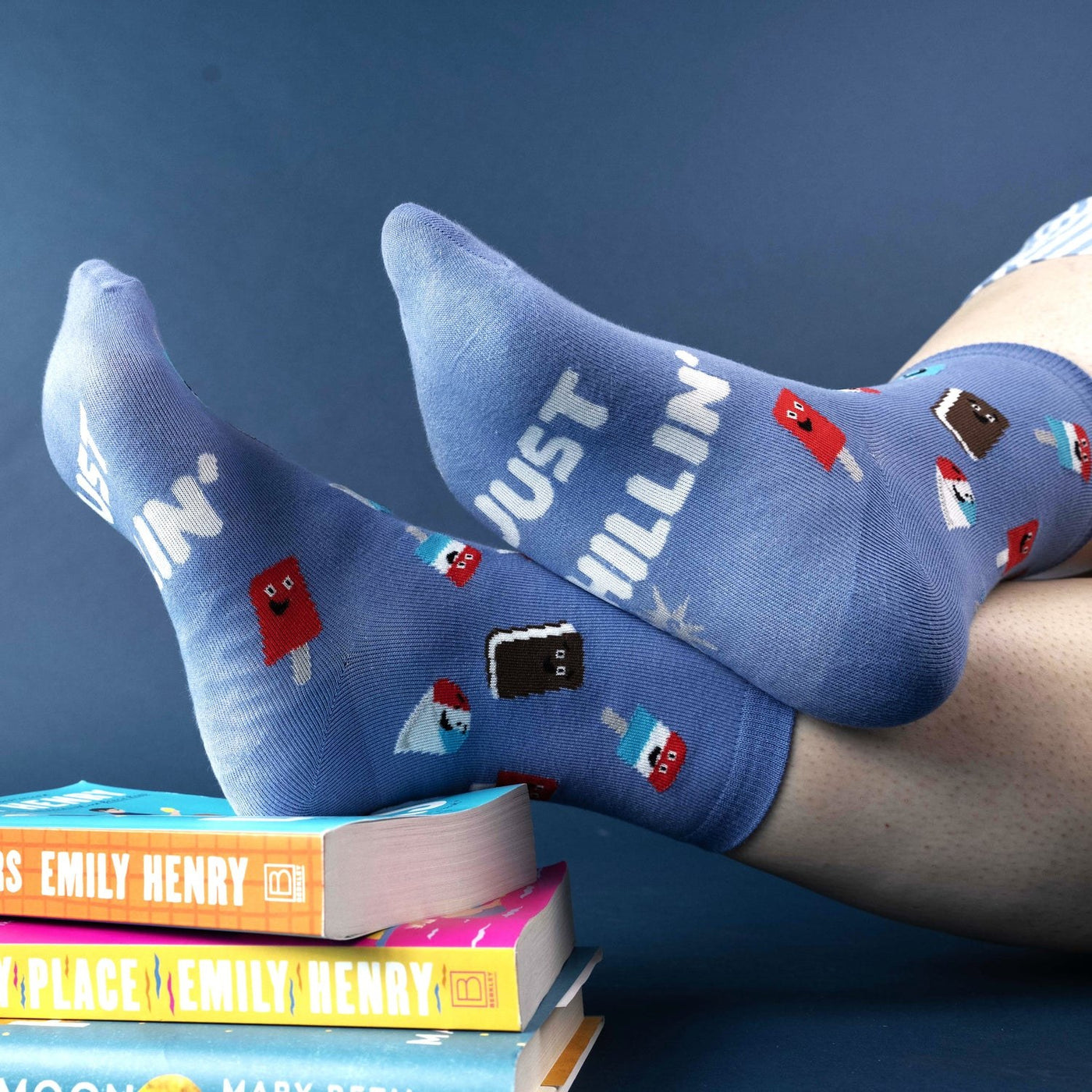 [lf] Feet in blue "Just Chillin'" socks with ice cream patterns resting on books.