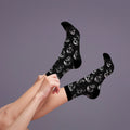 Lifestyle shot: a person adjusting the black skull socks on their legs. [lf]