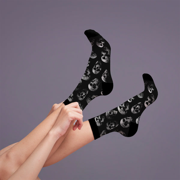 Lifestyle shot: a person adjusting the black skull socks on their legs. [lf]