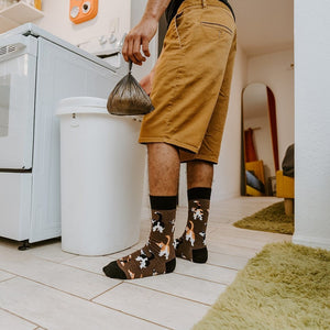 Holding a small trash bag inside an apartment, the wearer steps past a green shag rug while their Cat Butts socks in Brown Heather pop against pale tile, kitty tails arched mid-strut. [lf]