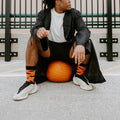 Wider rooftop frame of the same pumpkin perch, the model gazing off as Going Batty For Candy in Orange socks balance the orange gourd at his sneakers. [lf]
