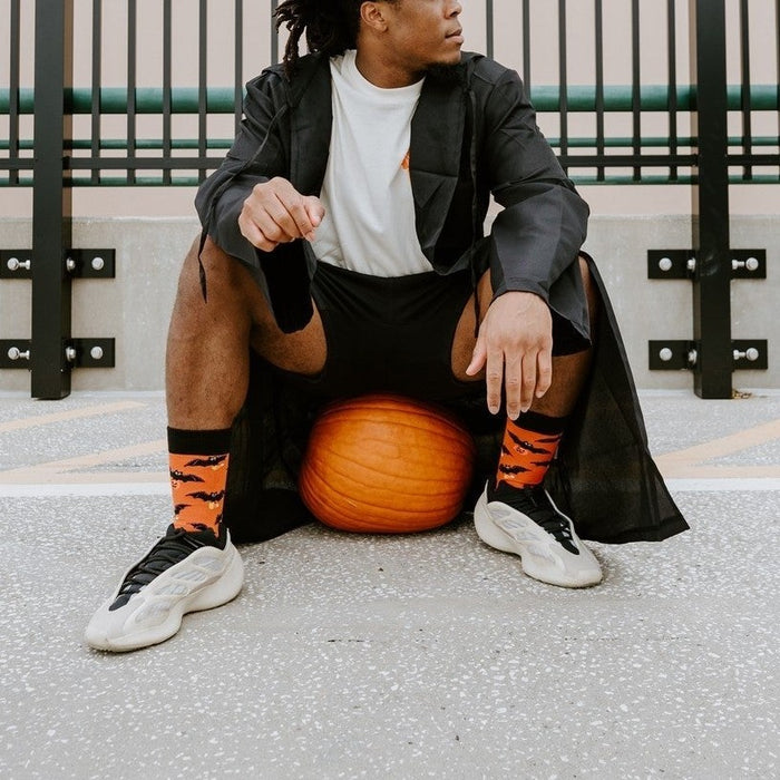 Wider rooftop frame of the same pumpkin perch, the model gazing off as Going Batty For Candy in Orange socks balance the orange gourd at his sneakers. [lf]