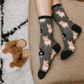 A woman crosses her legs on a wicker chair wearing Corgi Butt grey corgi socks and brown sandals. [lf]