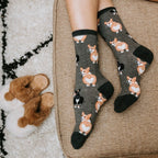A woman crosses her legs on a wicker chair wearing Corgi Butt grey corgi socks and brown sandals. [lf]