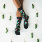 A friend hangs a glass pickle ornament on a tree, modeling Christmas Pickle socks in Black with playful graphics. [lf]