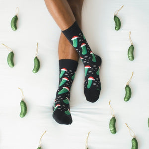 A friend hangs a glass pickle ornament on a tree, modeling Christmas Pickle socks in Black with playful graphics. [lf]