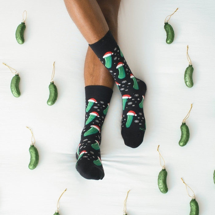 A friend hangs a glass pickle ornament on a tree, modeling Christmas Pickle socks in Black with playful graphics. [lf]