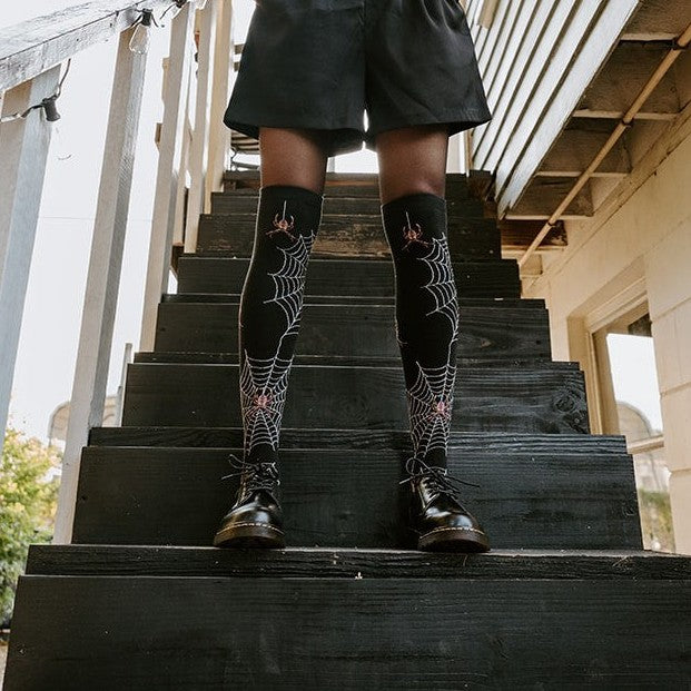 Spider Webs socks shown on a model standing on a sunlit garden staircase. [lf]