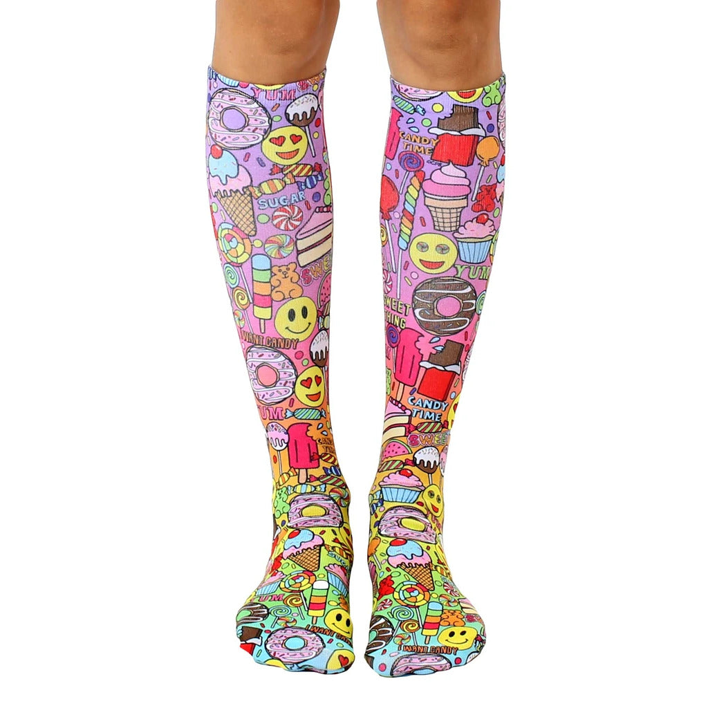 Knee-high socks with a colorful candy-themed print. Pink, purple, and yellow are prominent, featuring donuts, ice cream, and smiley faces. [lf]