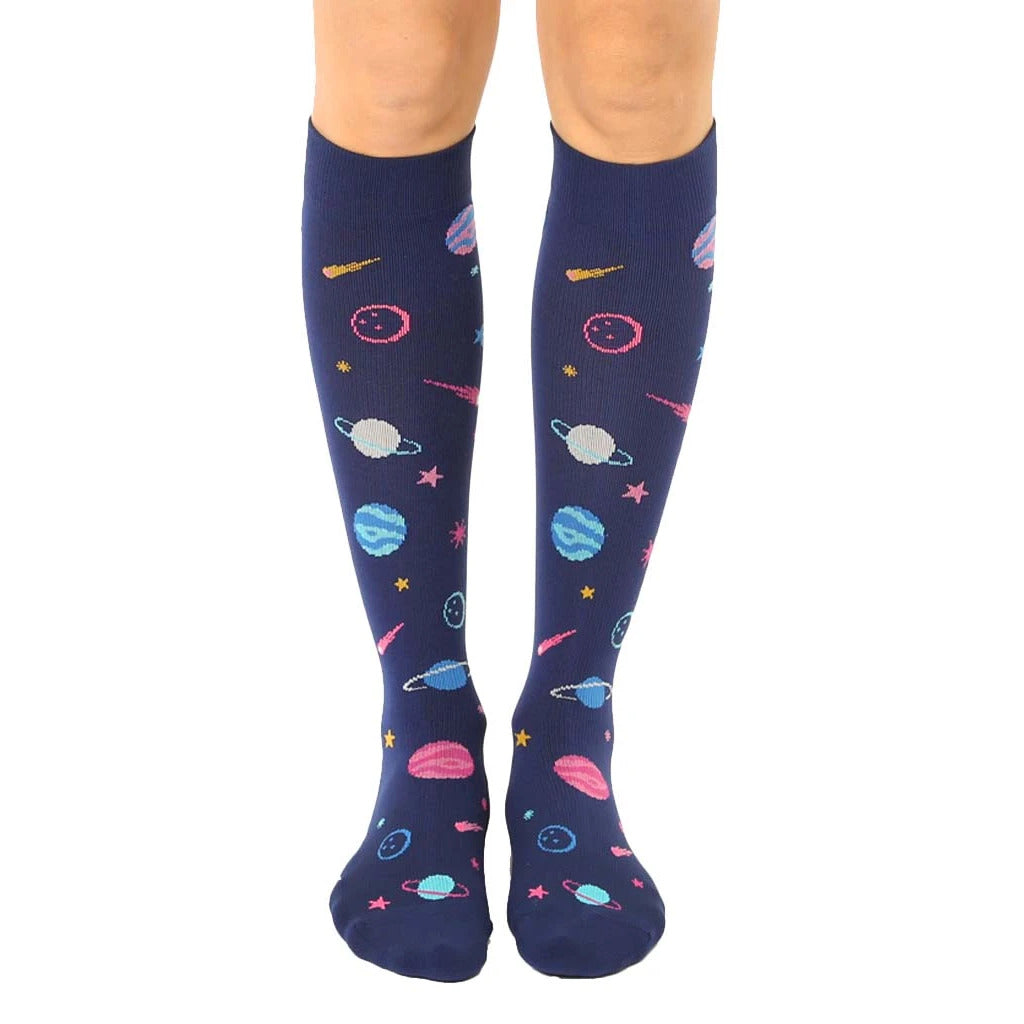 Knee-high navy blue compression socks with a whimsical pattern of planets, stars, and shooting stars in pink, teal, and yellow. [lf]