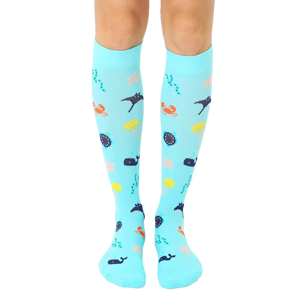 Pair of aqua blue knee-high compression socks.  A whimsical under-the-sea pattern with colorful whales, crabs, starfish, and stingrays is shown. [lf]