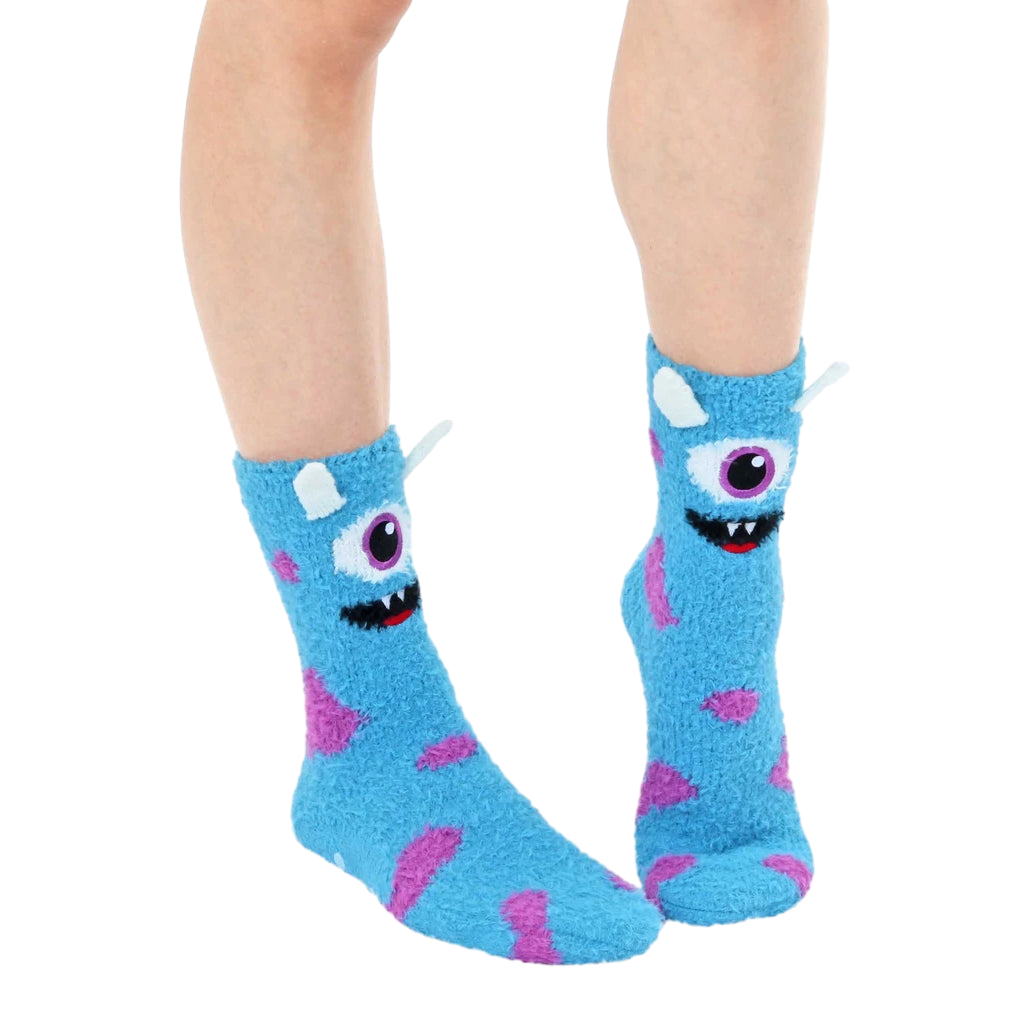 Lifestyle shot of light blue fuzzy monster slipper socks worn on a person's feet. [lf]