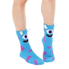 Lifestyle shot of light blue fuzzy monster slipper socks worn on a person's feet. [lf]
